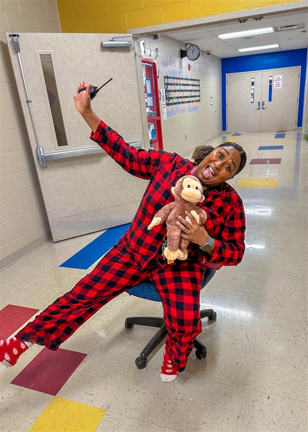 principal in red pajamas on a chair in the hallway with monkey stuffed animal 